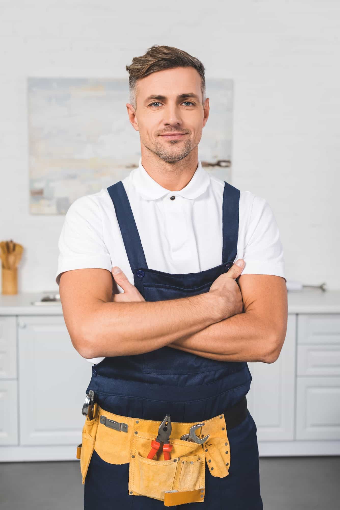 adult-repairman-in-tool-belt-standing-with-crossed-arms-at-kitchen-and-looking-at-camera.jpg